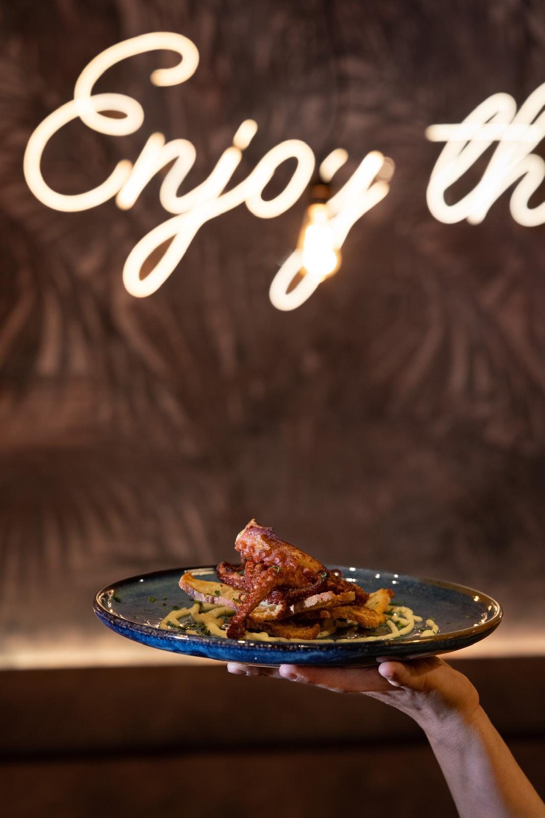 Polpo croccante servito davanti alla scritta al neon di Enjoy Fish